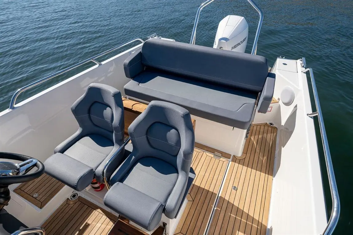 Two grey seats and a backrest on a boat deck, with wooden flooring and a visible Mercury engine against a water background.